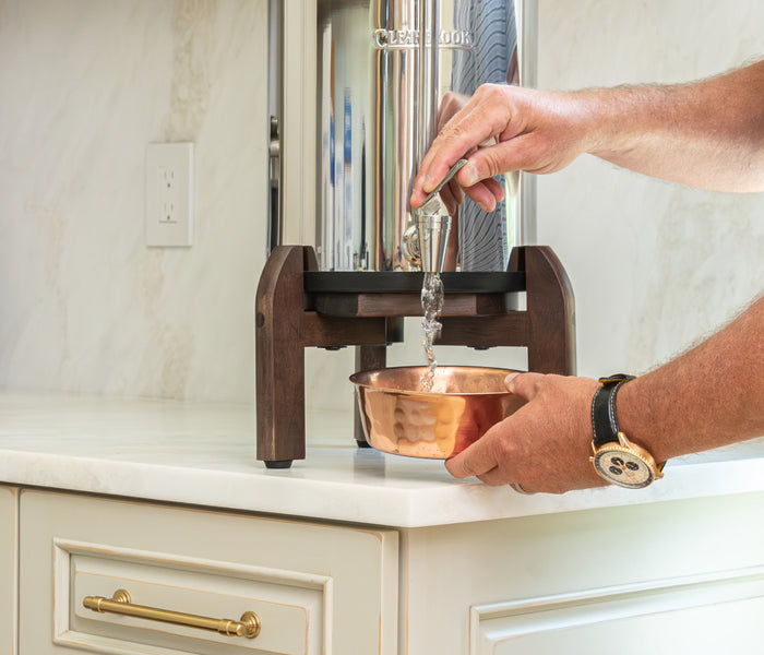 Hands filling a dog bowl from the spigot of a Clearbrook gravity filter system