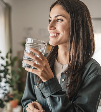 woman drinking a glass of filtered water beside a kitchen window